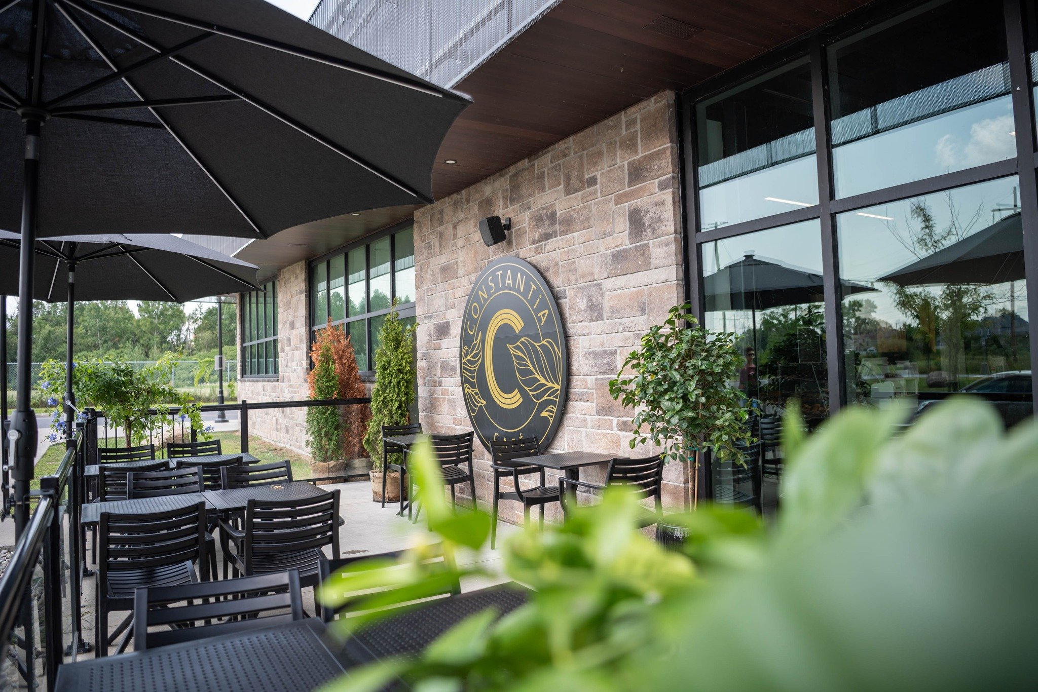 Terrasse d'été du Café Constantia avec logo mural et végétation